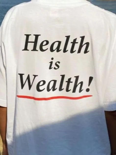 Person from behind wearing a white T-shirt printed with the phrase 'Health is Wealth!'