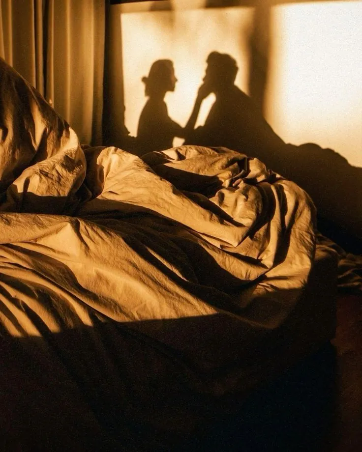 Sunlight casting the shadow of a couple holding hands against a wall behind a bed