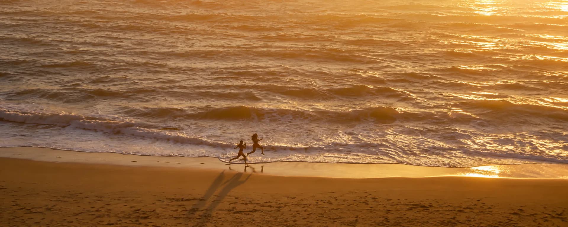 Two people running along the shoreline at sunset, seen from above