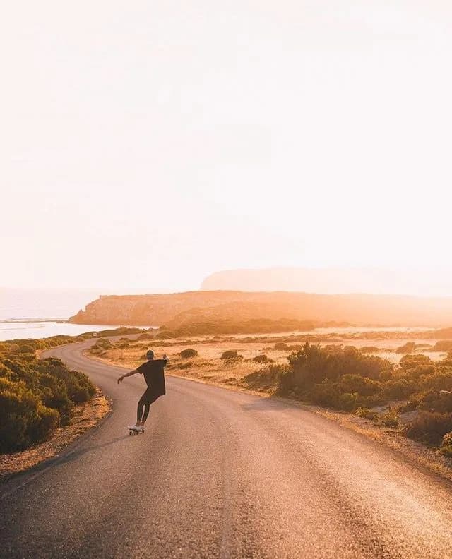 A skateboarder riding a winding coastal road at golden hour