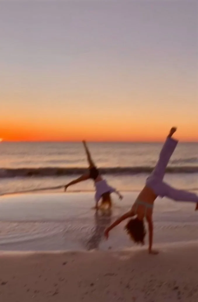 Two people cartwheeling on the beach at sunset
