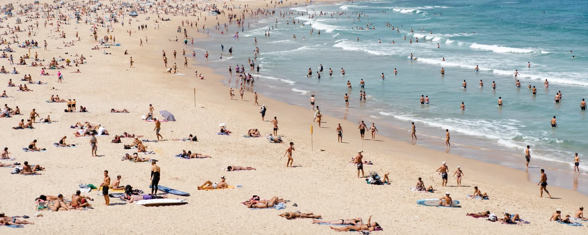 Aerial view of a crowded Bondi Beach, sunbathers across the sand and swimmers in the surf
