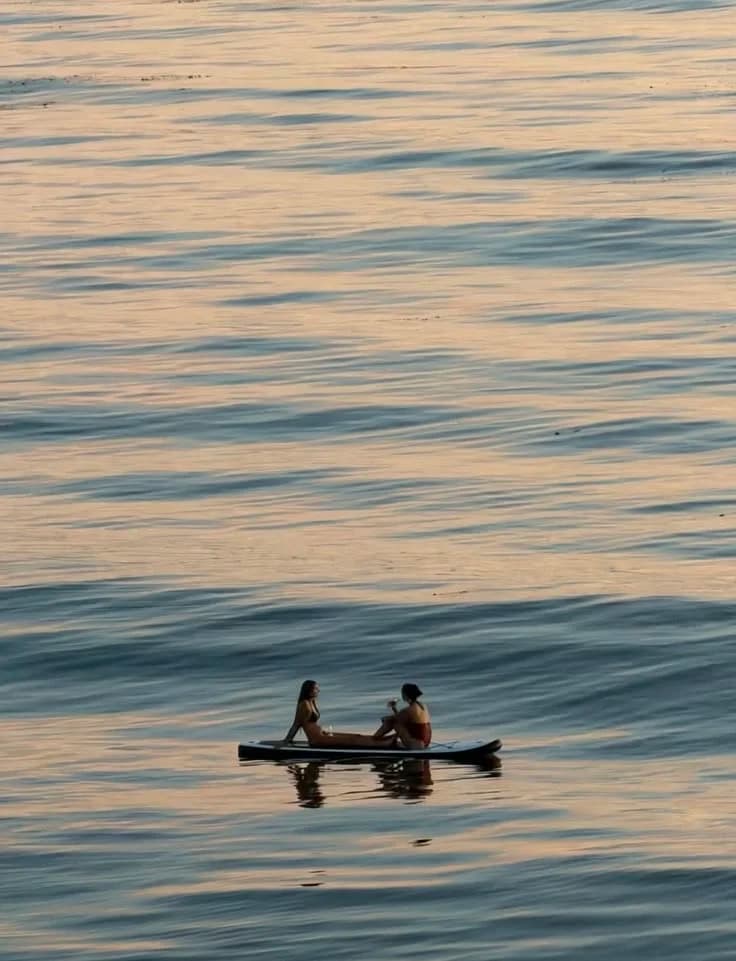 Two people relaxing on a paddleboard on calm golden water